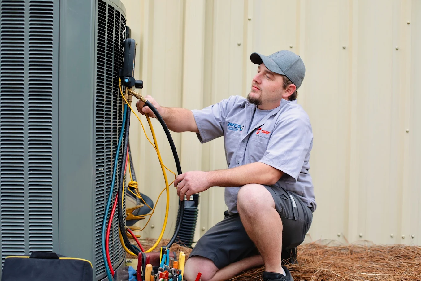 Technician inspecting HVAC unit with gauges outdoors.